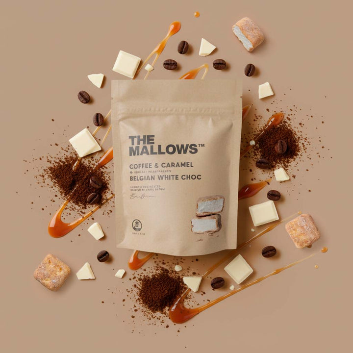 The Mallows coffee and caramel Belgian white choc packaging surrounded by chocolate pieces and coffee beans on a brown background.