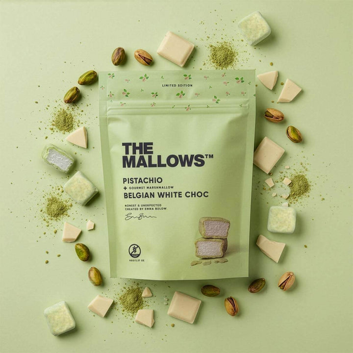 Packaging of 'The Mallows' pistachio Belgian white choc marshmallows on a green background with marshmallows and pistachios around.