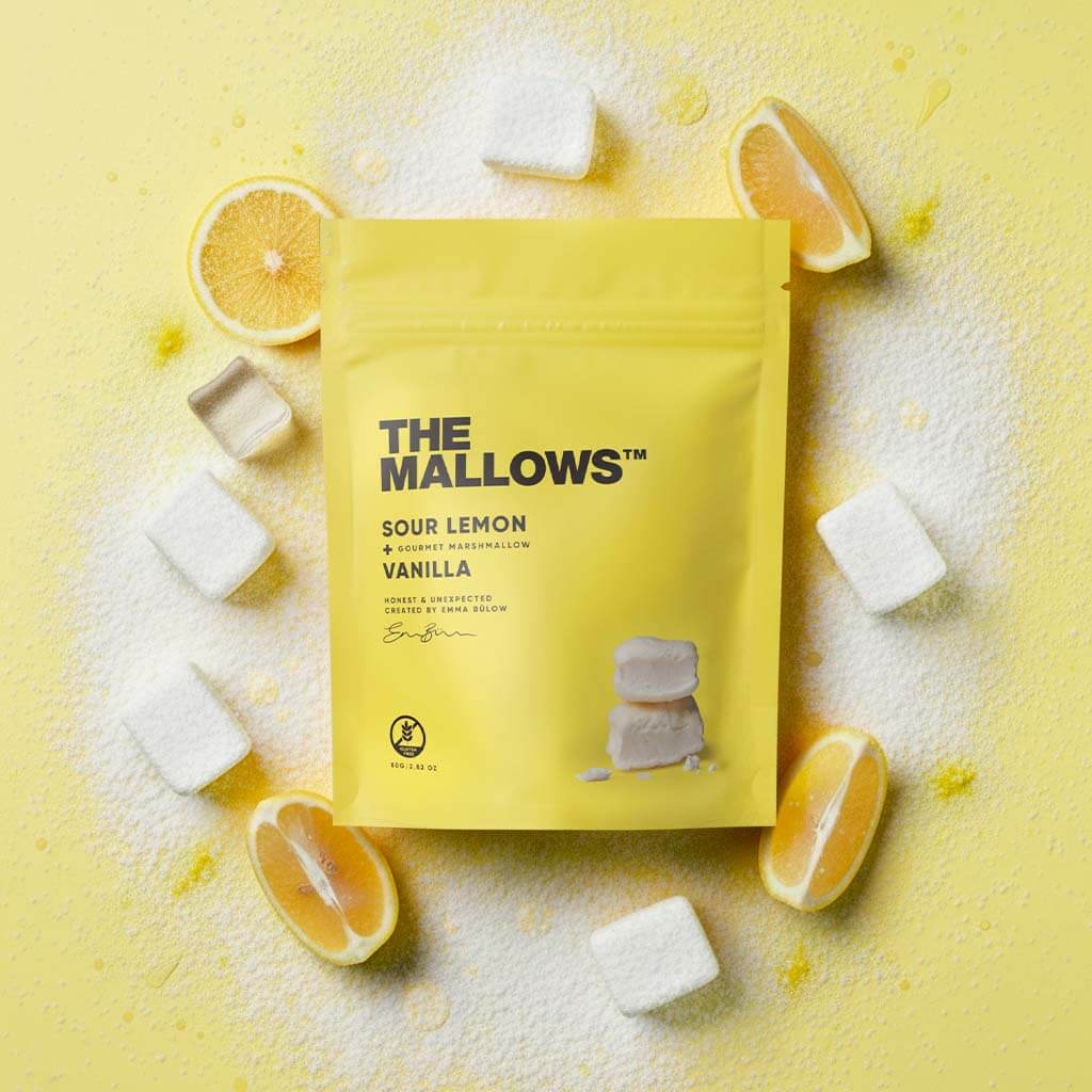 Yellow package of 'The Mallows' Sour Lemon Vanilla marshmallows on a yellow background with lemon slices and marshmallows.