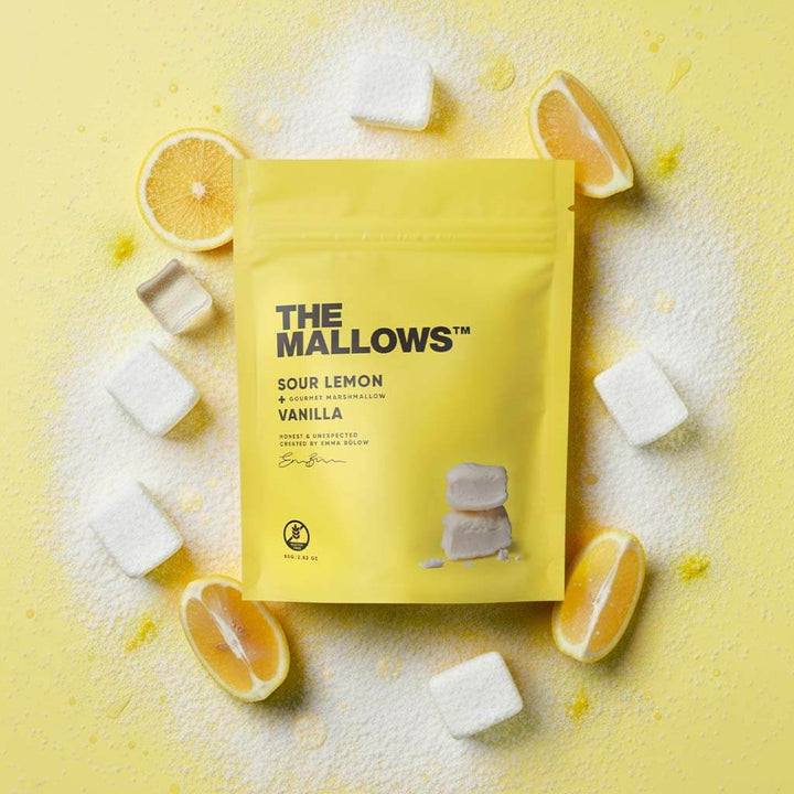 Yellow package of 'The Mallows' Sour Lemon Vanilla marshmallows on a yellow background with lemon slices and marshmallows.